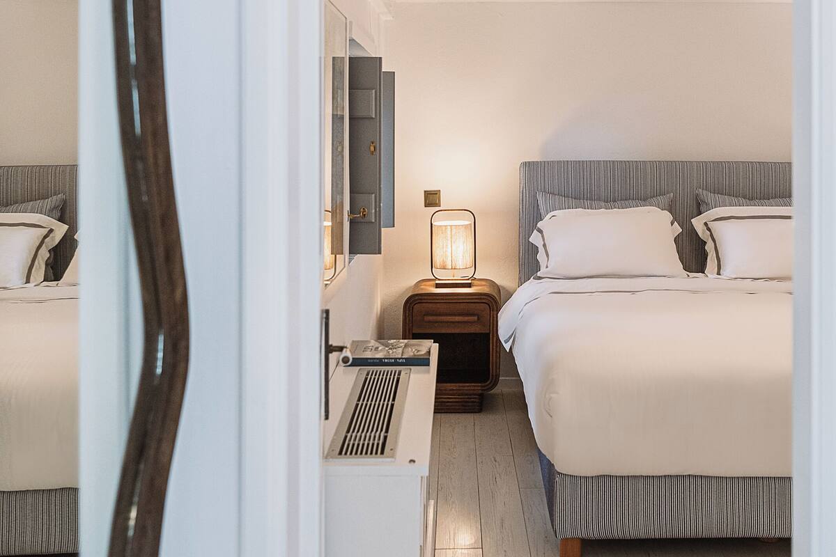 Una habitación de hotel con cama, mesita de noche, lámpara y espejo.