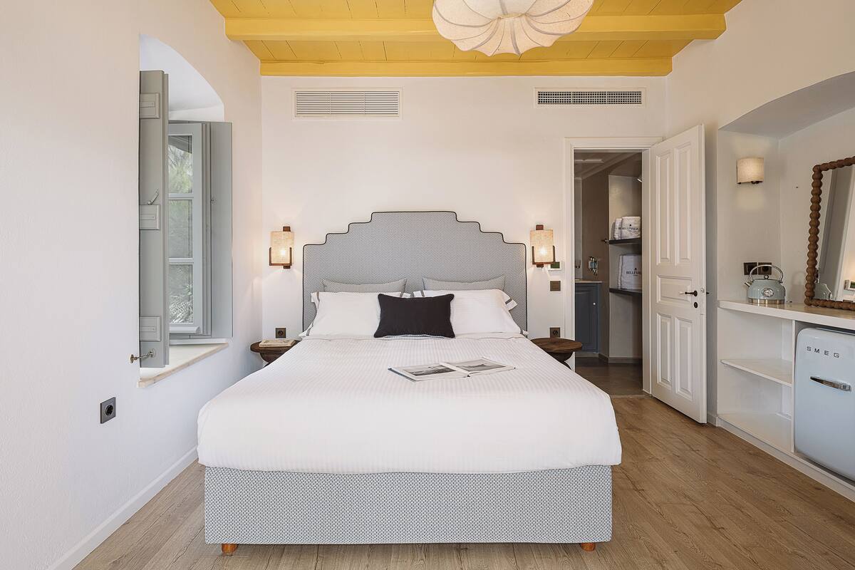 Un dormitorio con una cama grande, lámparas de noche, techo de madera y vista al baño.