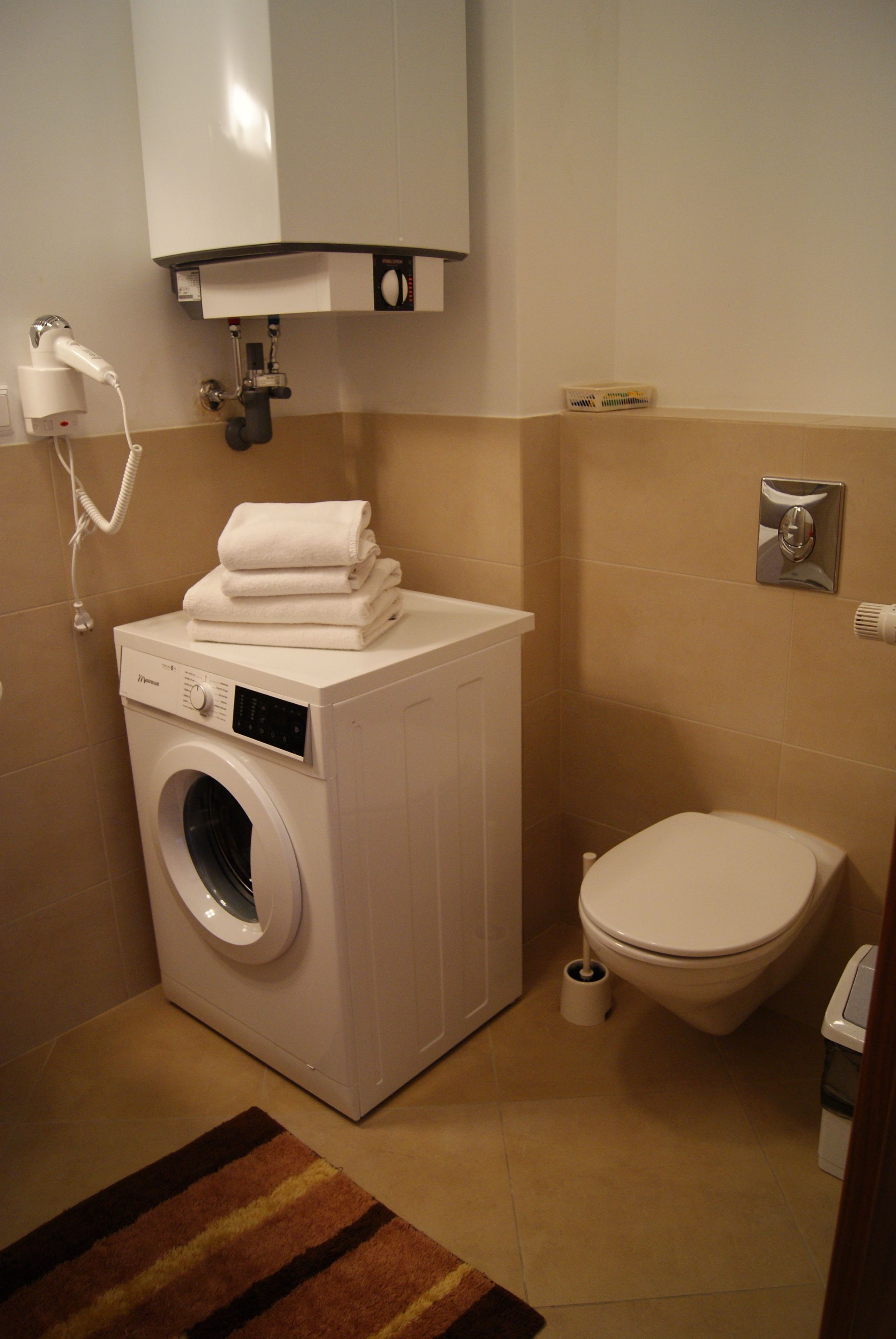 A compact bathroom with a washing machine, toilet, and a towel rack.