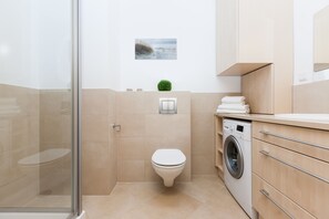 A modern bathroom with a glass shower enclosure, a toilet, a washing machine, and a small wall-mounted sink. - Aquamarina (Miedzyzdroje)
