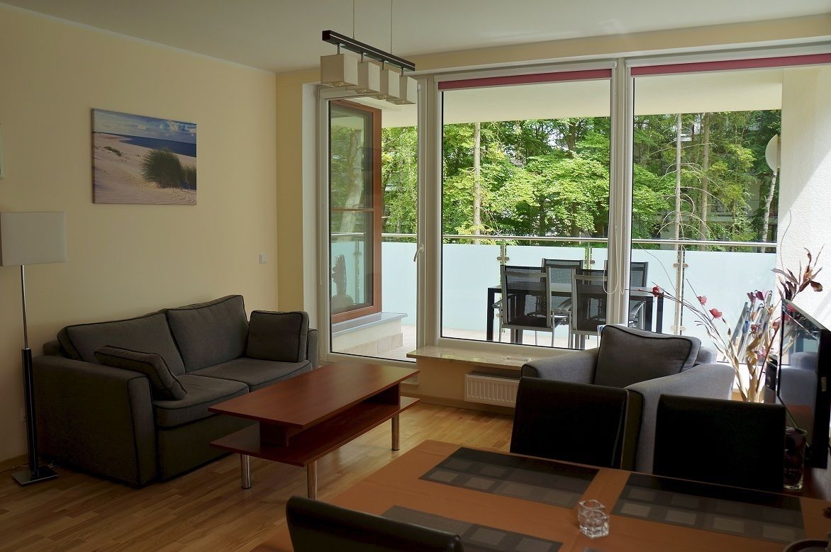 Un salon moderne comprenant un canapé, une table basse et un coin repas. De grandes fenêtres offrent une vue sur la verdure environnante.