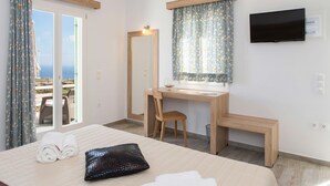 A hotel room with a bed, a desk, a chair, a TV, and a view of the sea. - Rooms & Apartments Archontou (Sifnos)