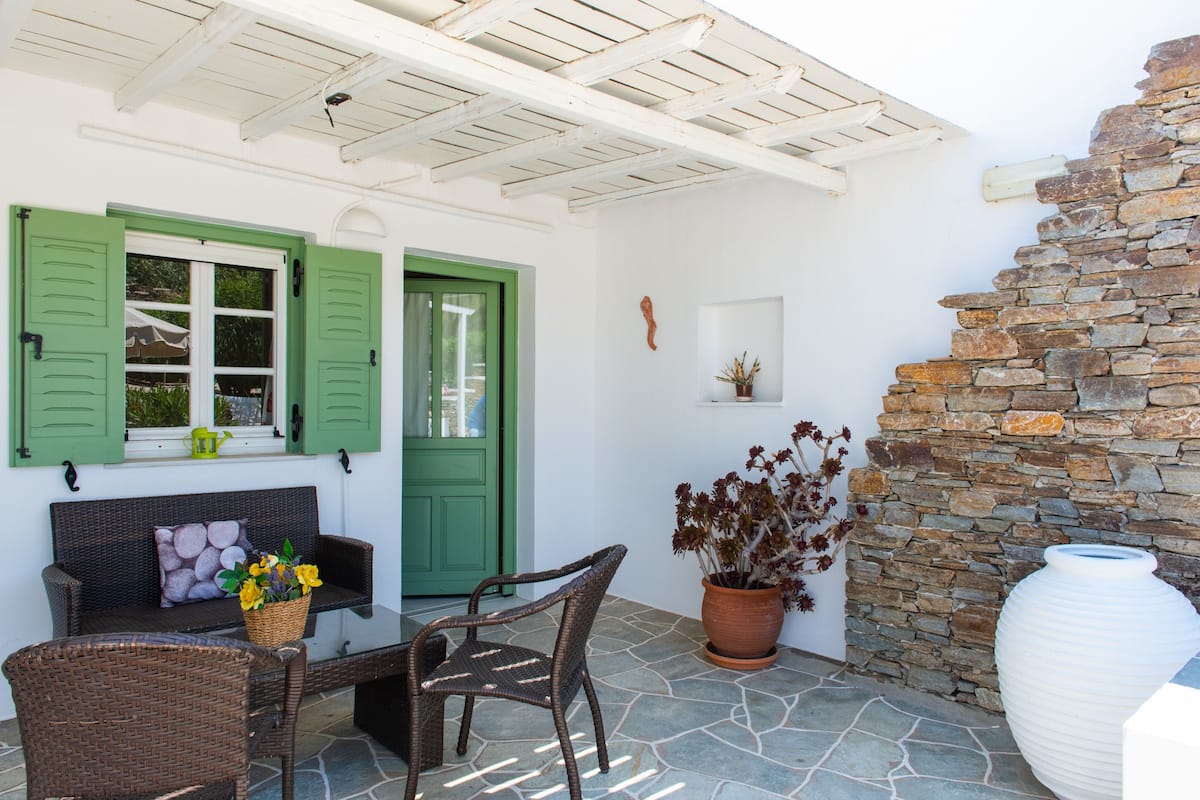 Un patio con un sofá de mimbre, una mesa de comedor, sillas, una planta en maceta y un muro de piedra.