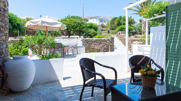 An outdoor patio with stone flooring, wicker furniture, and a table with a basket of flowers. - Rooms & Apartments Archontou (Sifnos)