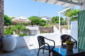 An outdoor patio with stone flooring, wicker furniture, and a table with a basket of flowers. - Rooms & Apartments Archontou (Sifnos)