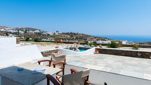 A terrace with stone flooring, a pool, and a view of a coastal village. - Rooms & Apartments Archontou (Sifnos)