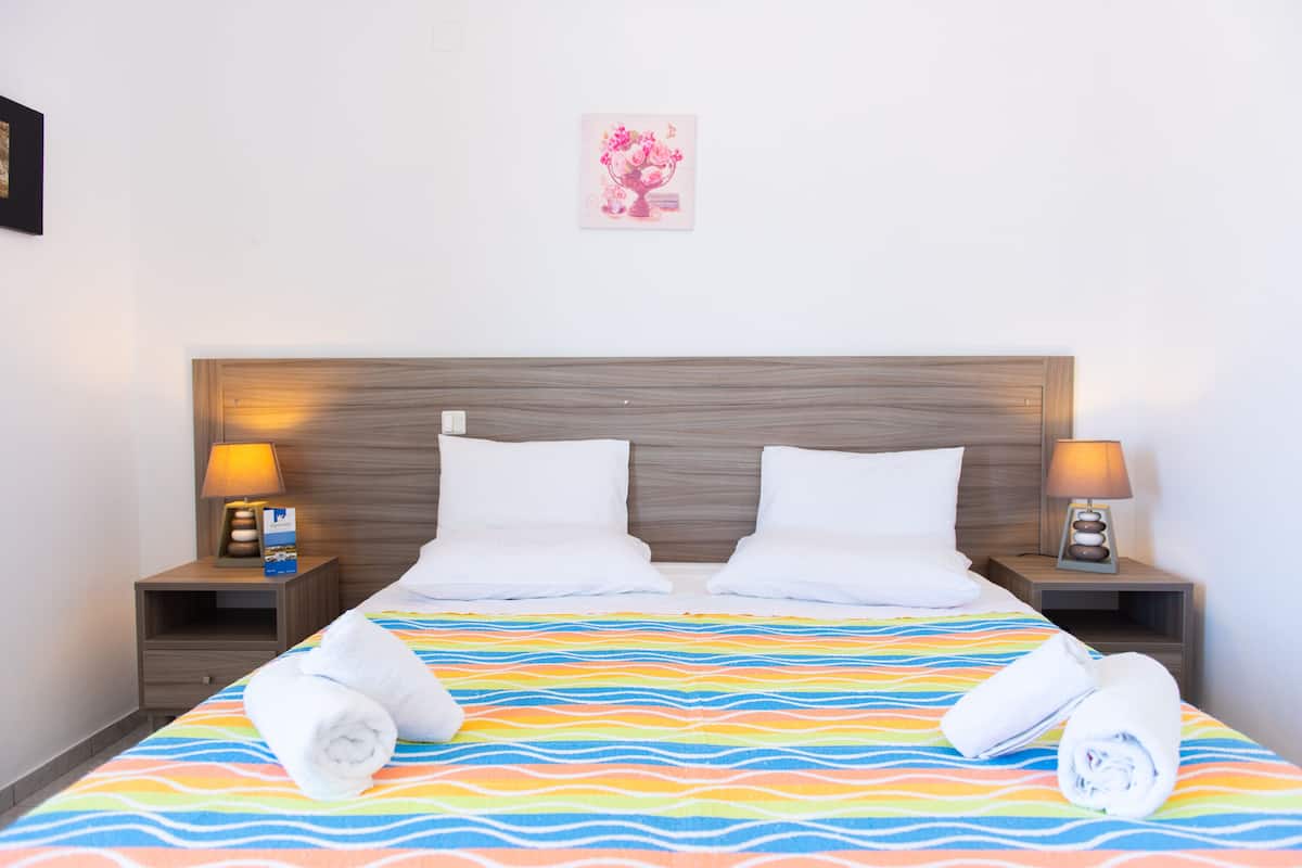 Habitación de hotel con cabecera de madera, dos almohadas blancas, colcha de rayas de colores y dos lámparas de noche.