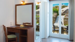 A room with a wooden desk, a chair, a large mirror, and a sliding glass door leading to an outdoor area with a stone staircase and a table. - Rooms & Apartments Archontou (Sifnos)