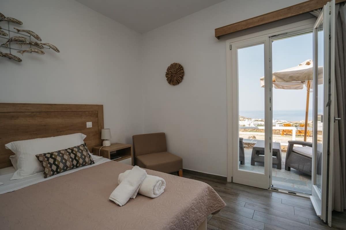 Habitación de hotel con cama, una silla, mesita de noche, lámpara y vistas al exterior.