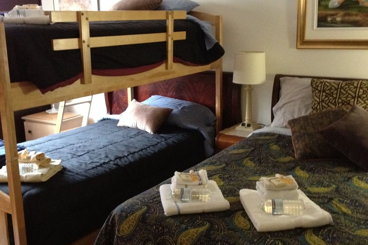A hotel room with two bunk beds, a patterned bedspread, a bedside table with a lamp, and a framed picture on the wall.