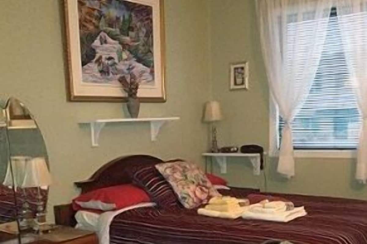 A bedroom with a bed, a dresser, a desk, a chair, a lamp, a painting on the wall, and a window with curtains.