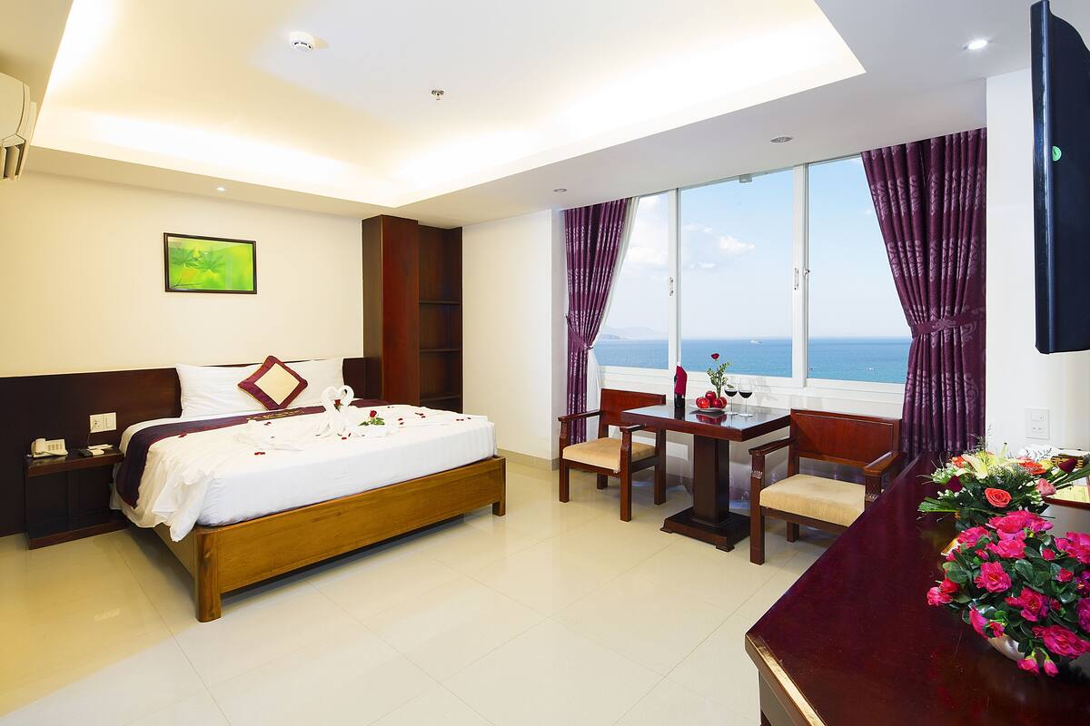 Ein Hotelzimmer mit Bett, Schreibtisch, Stuhl, Fenster mit Meerblick und einem Bild an der Wand.