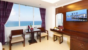 A hotel room with a large window, a wooden desk, a television, and a view of the sea. - Majestic Nha Trang Hotel (Nha Trang)