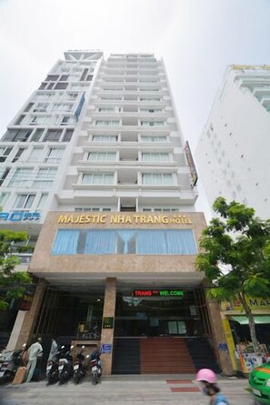 Ett hotell med en modern fasad, en framträdande entré och en skylt med texten ”MAJESTIC NHATTRANG HOTEL”.