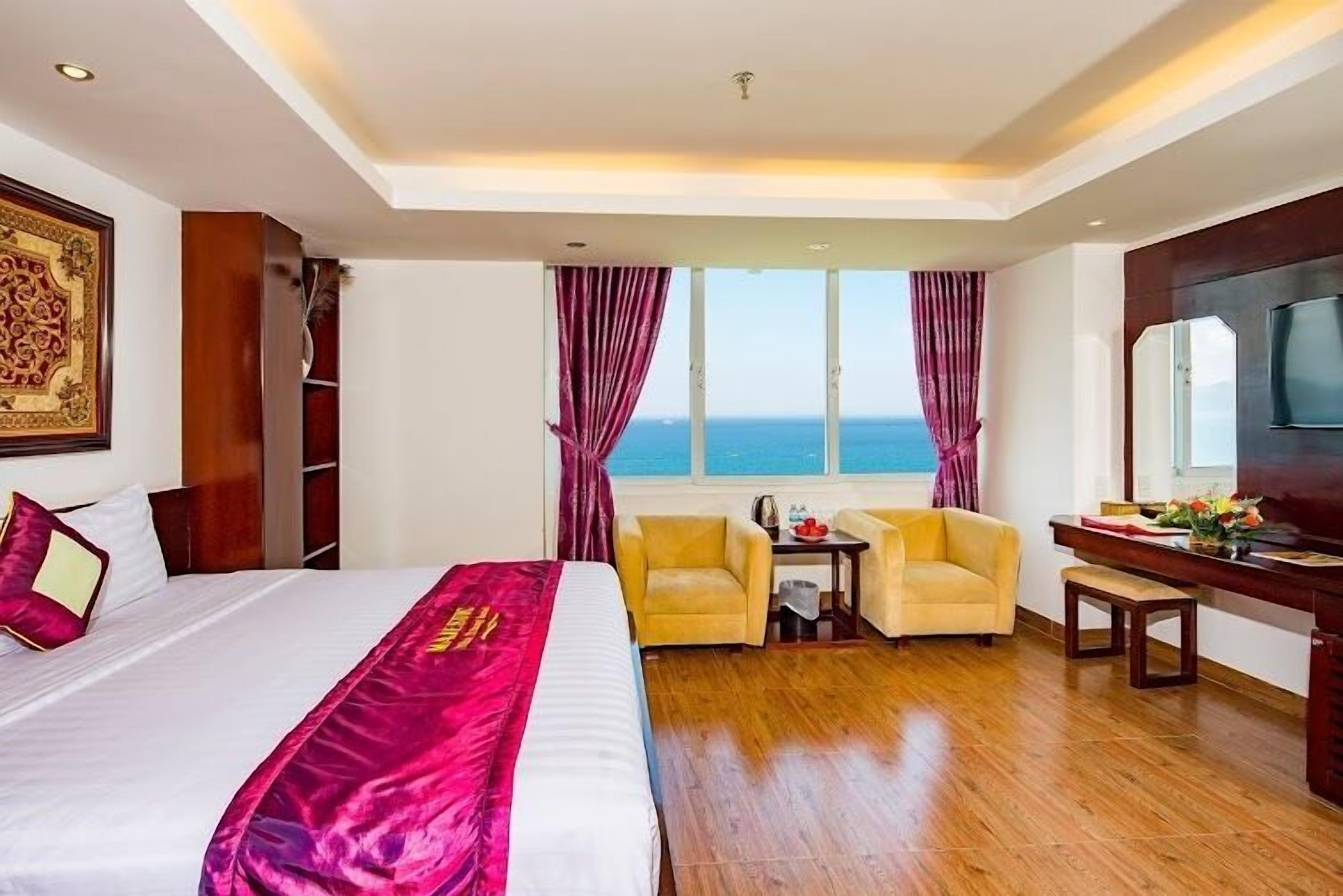 A hotel room with a large bed, two armchairs, a desk, and a view of the sea.