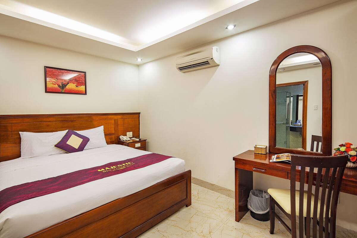 Ein Hotelzimmer mit einem Holzbett, einem Schreibtisch, einem Sessel, einem Spiegel und einer Wandklimaanlage.