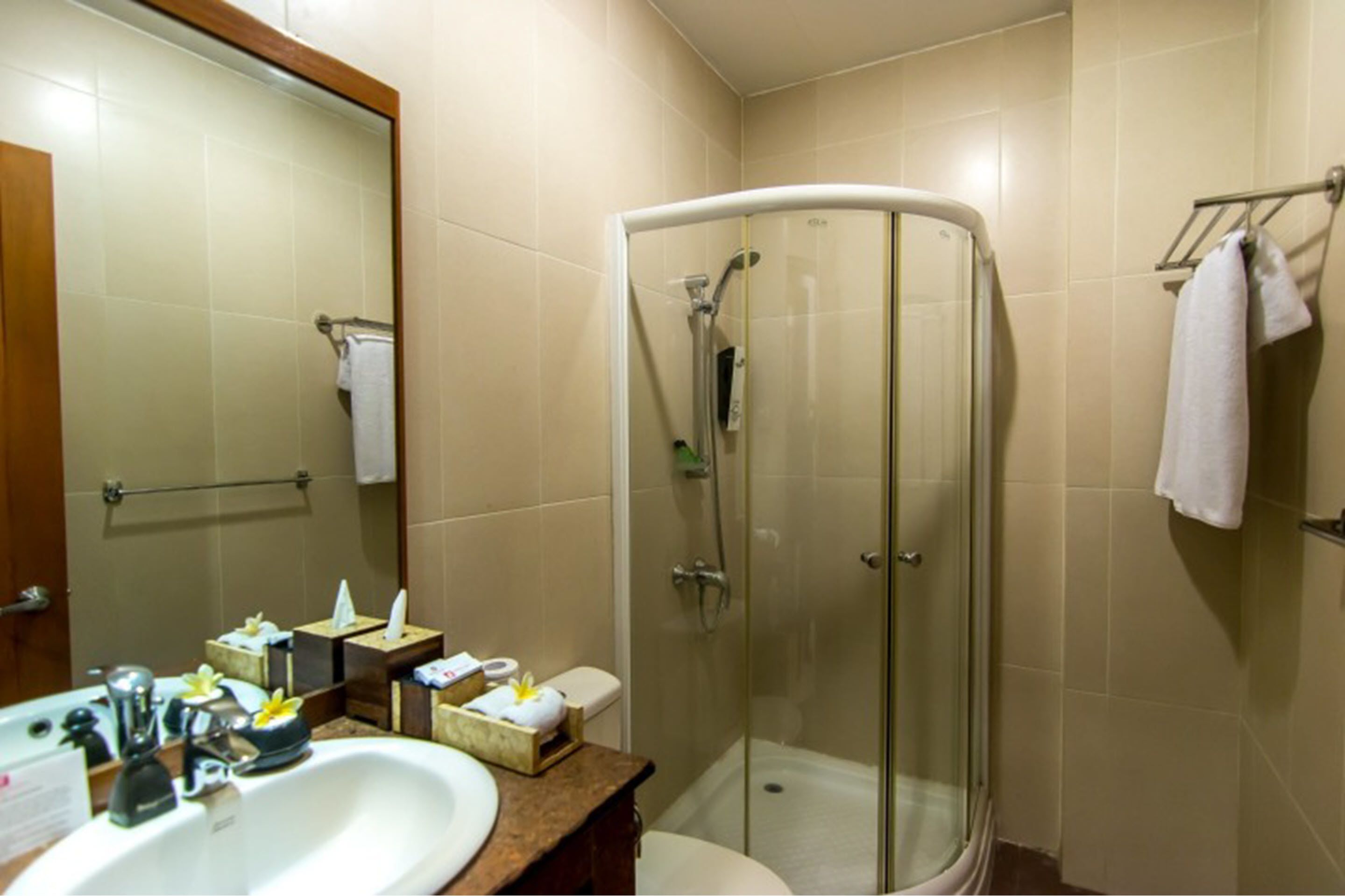 A bathroom with a glass-enclosed shower, a sink with toiletries, and a mirror.