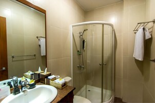 Un baño con ducha de vidrio, un lavamanos con artículos de aseo y un espejo.