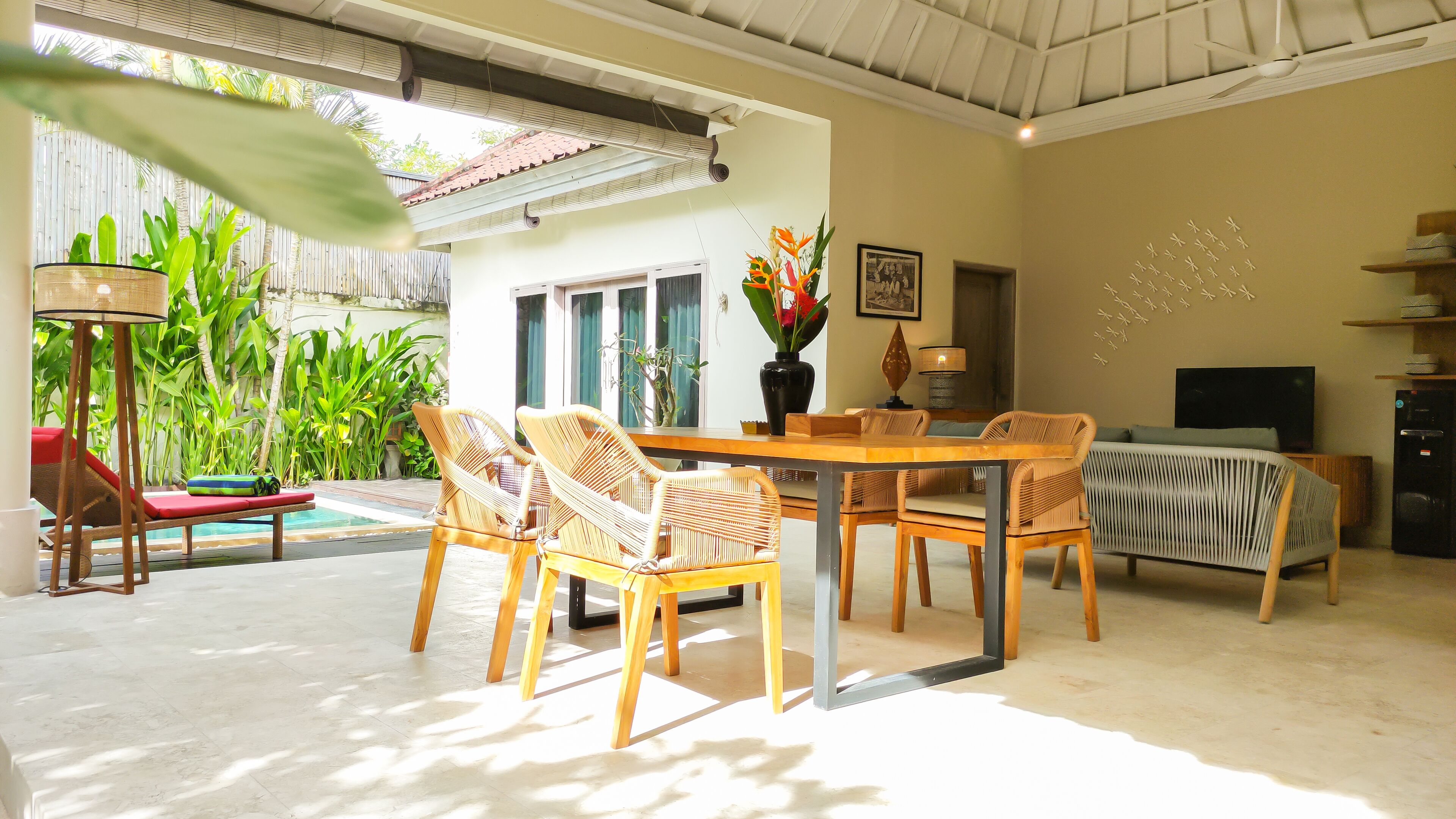 A spacious living area with a dining table, wicker chairs, a sofa, a TV, and a pool.