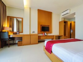 Quarto de hotel com cama, escrivaninha, televisão e ar condicionado.