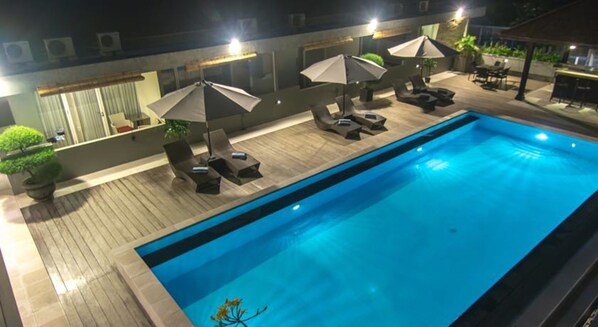 Una piscina con sillas de descanso y sombrillas, rodeada por una terraza de madera y plantas en macetas.