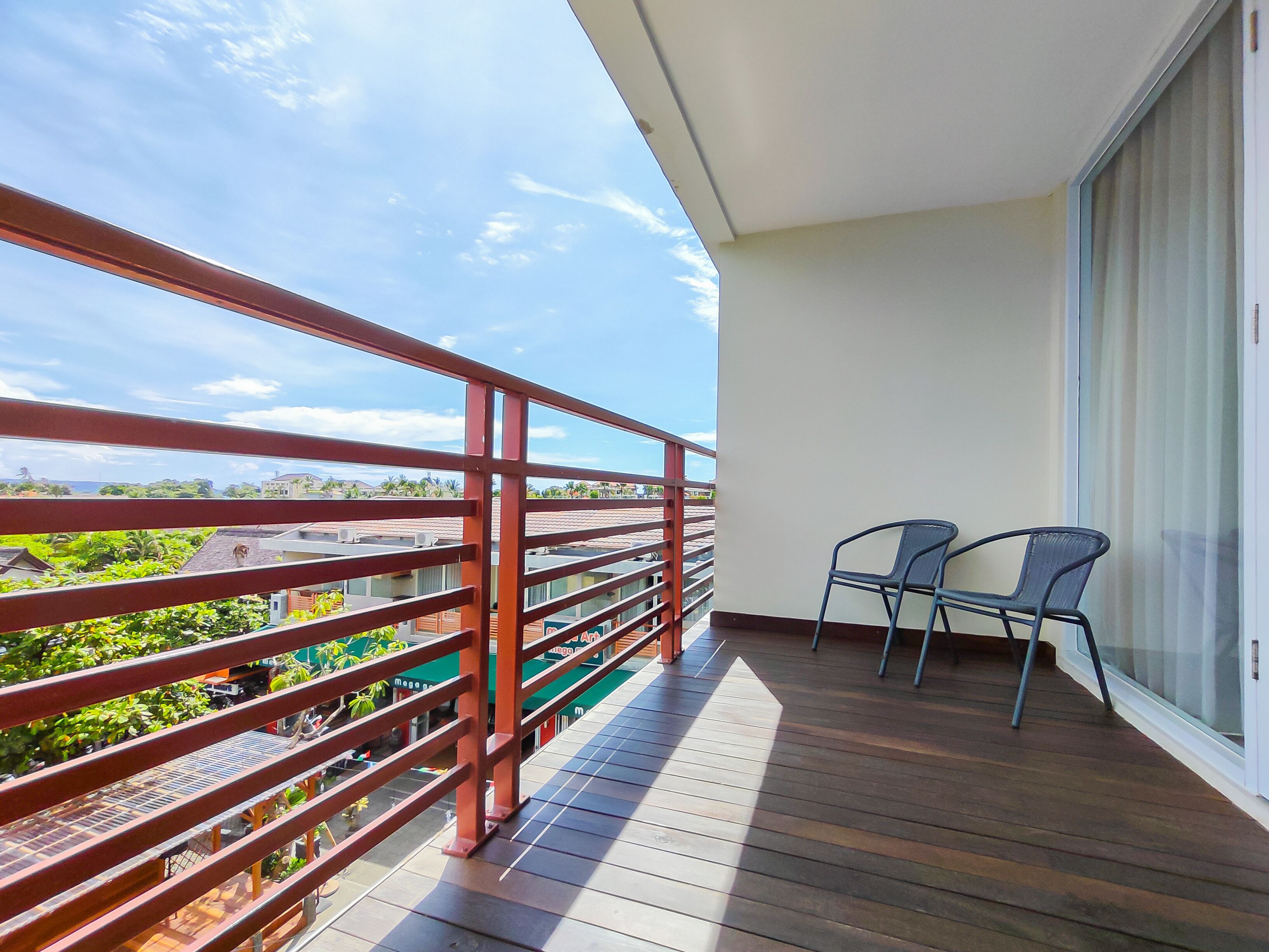 A balcony with a wooden floor, a red metal railing, and two chairs.