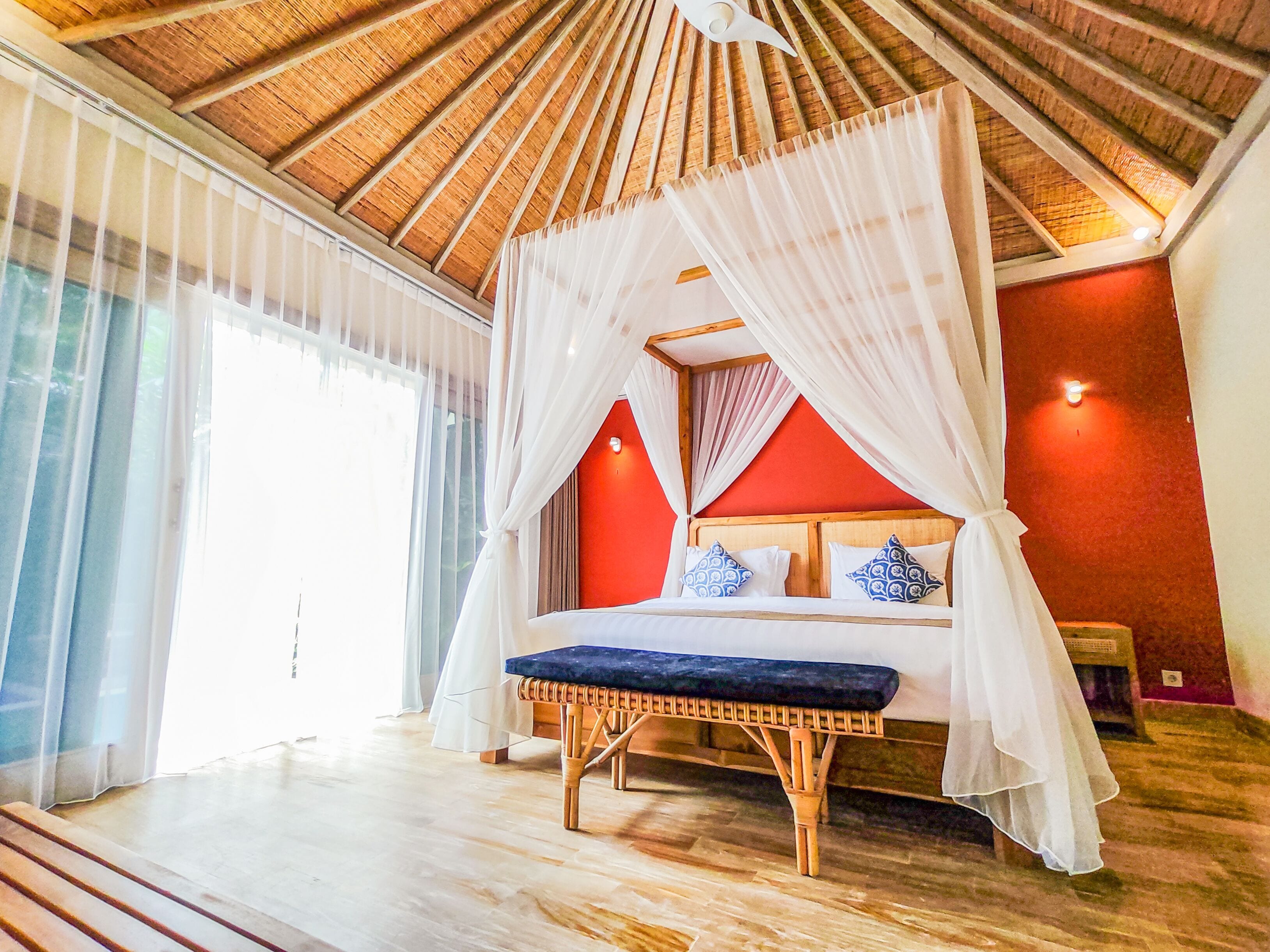A room with a bed under a canopy, a wooden ceiling, and a red wall.