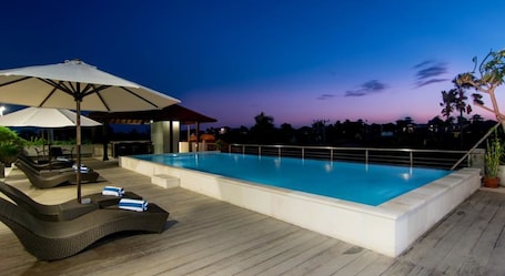 Una piscina al aire libre, sombrillas, sillones reclinables de piscina