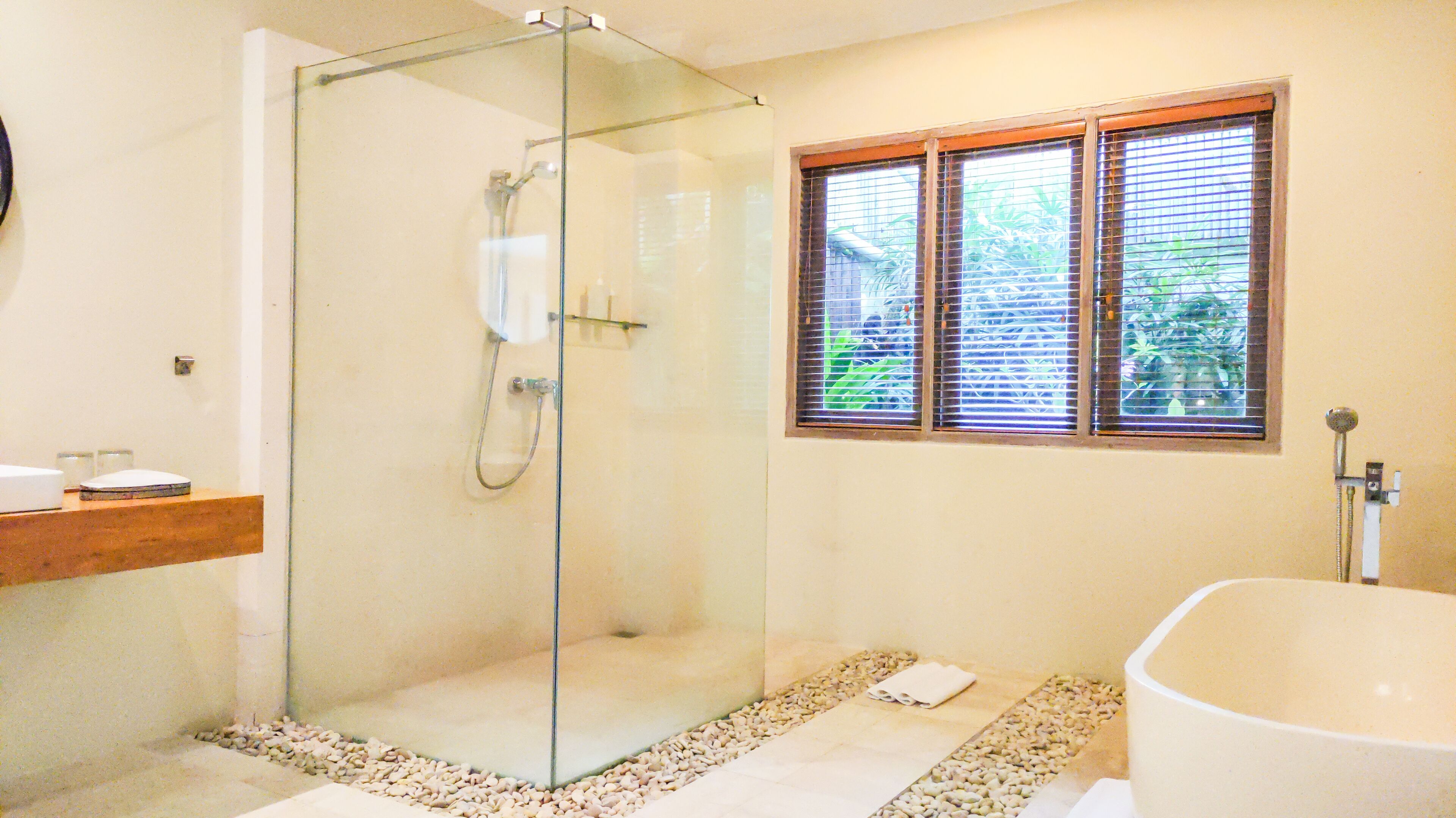 Un baño moderno con ducha de vidrio, una bañera independiente y una ventana con persianas.
