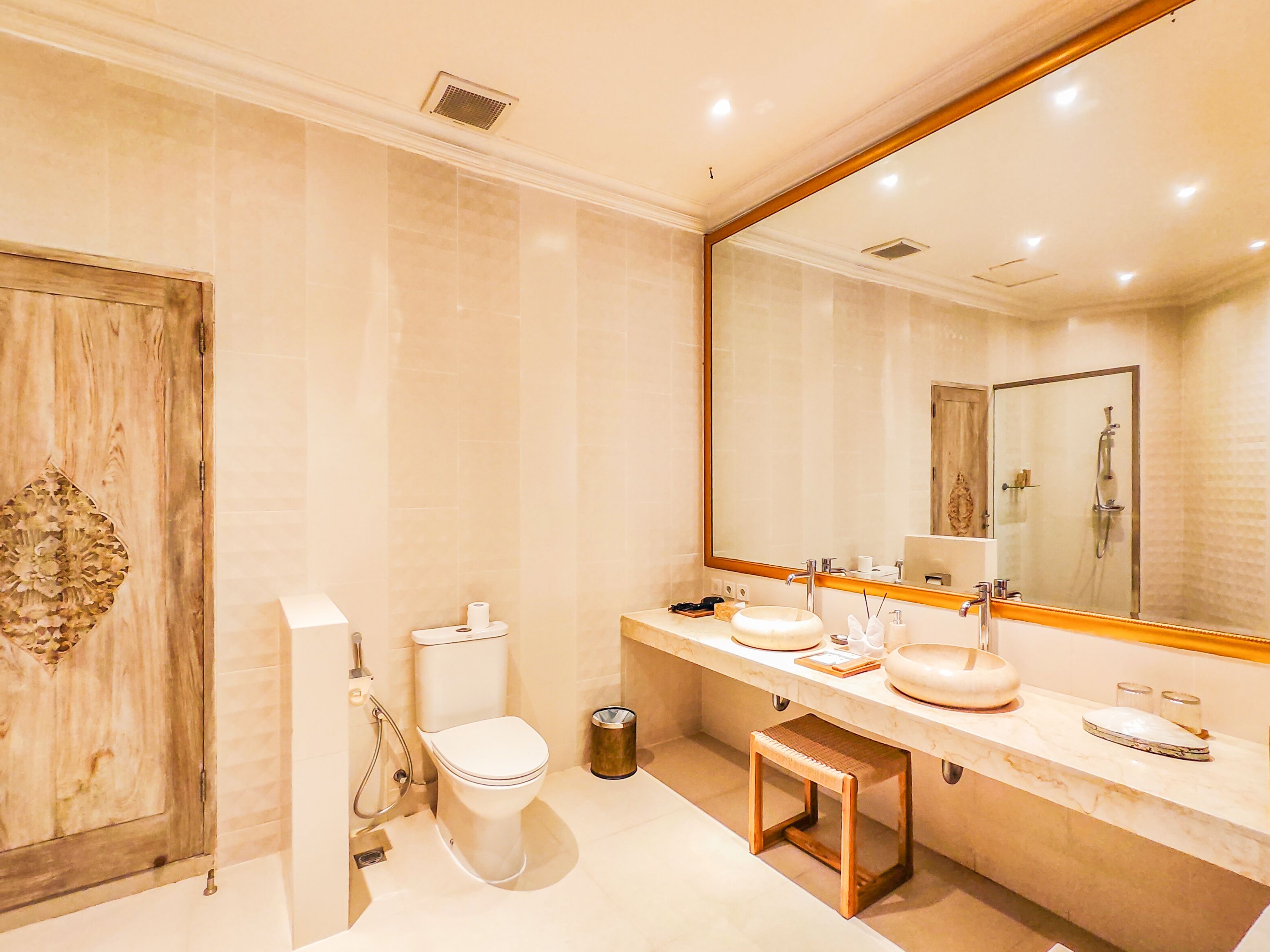 A modern bathroom with a wooden door, a toilet, a sink with a mirror, and a shower area.