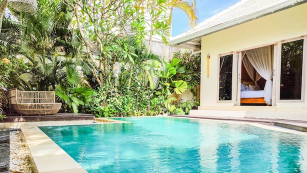 Una piscina con agua azul cristalina, rodeada de vegetación exuberante y un sofá de mimbre.