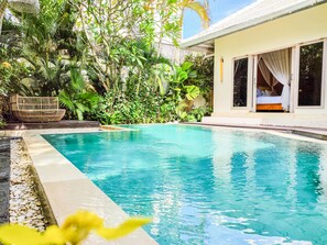 Una piscina con agua azul cristalina, rodeada de vegetación exuberante y un sofá de mimbre.