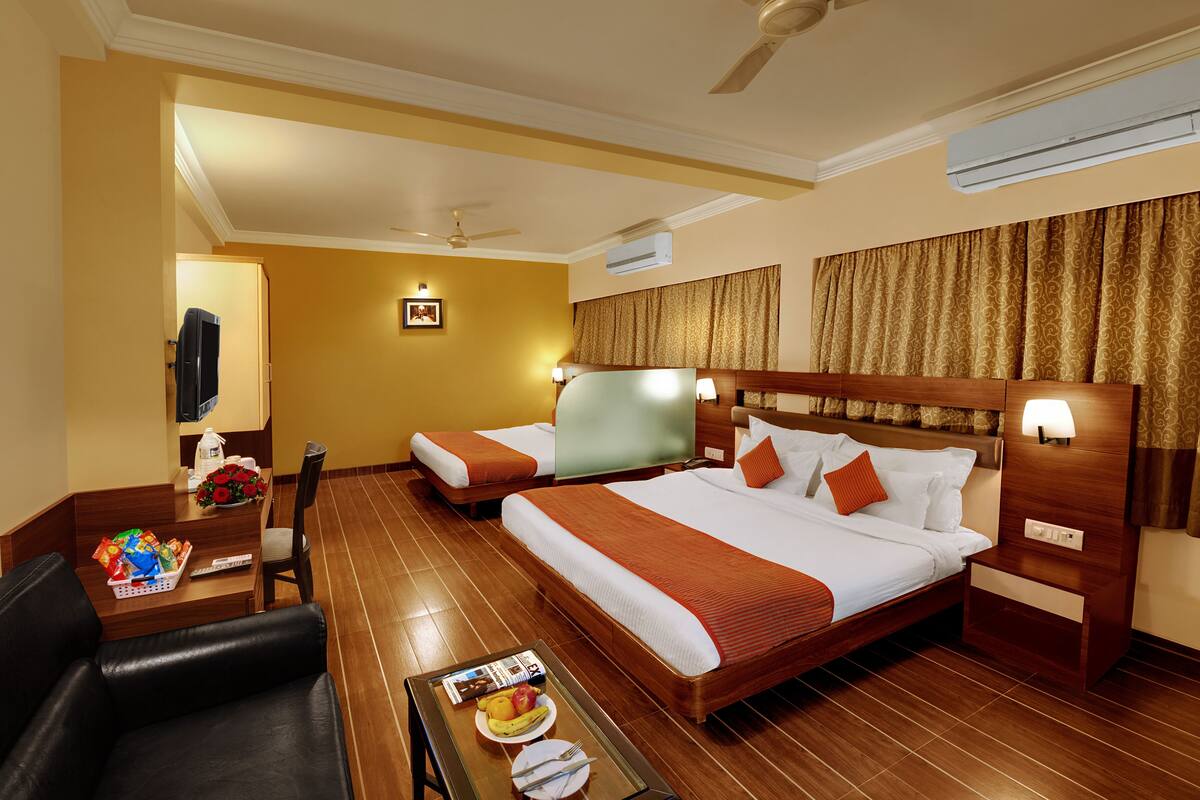 A hotel room with two beds, a desk, a chair, a small table with breakfast items, and an air conditioning unit.