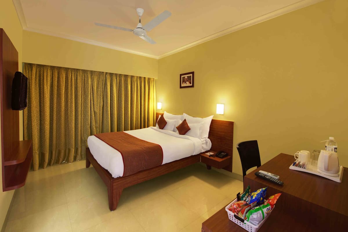 A hotel room with a bed, bedside table, nightstand, and a desk with a chair.