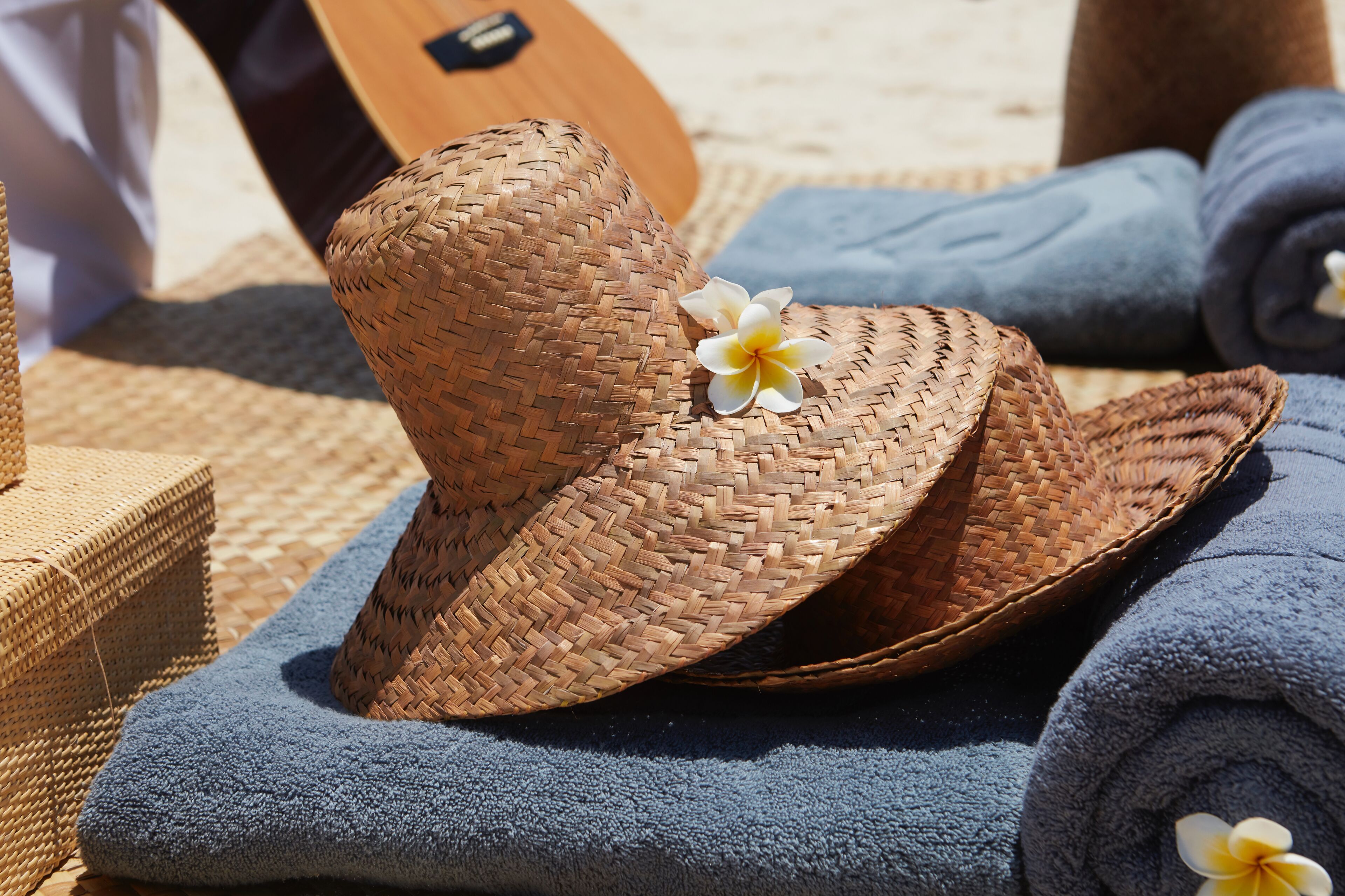 A woven straw hat with a flower, placed on a blue towel.