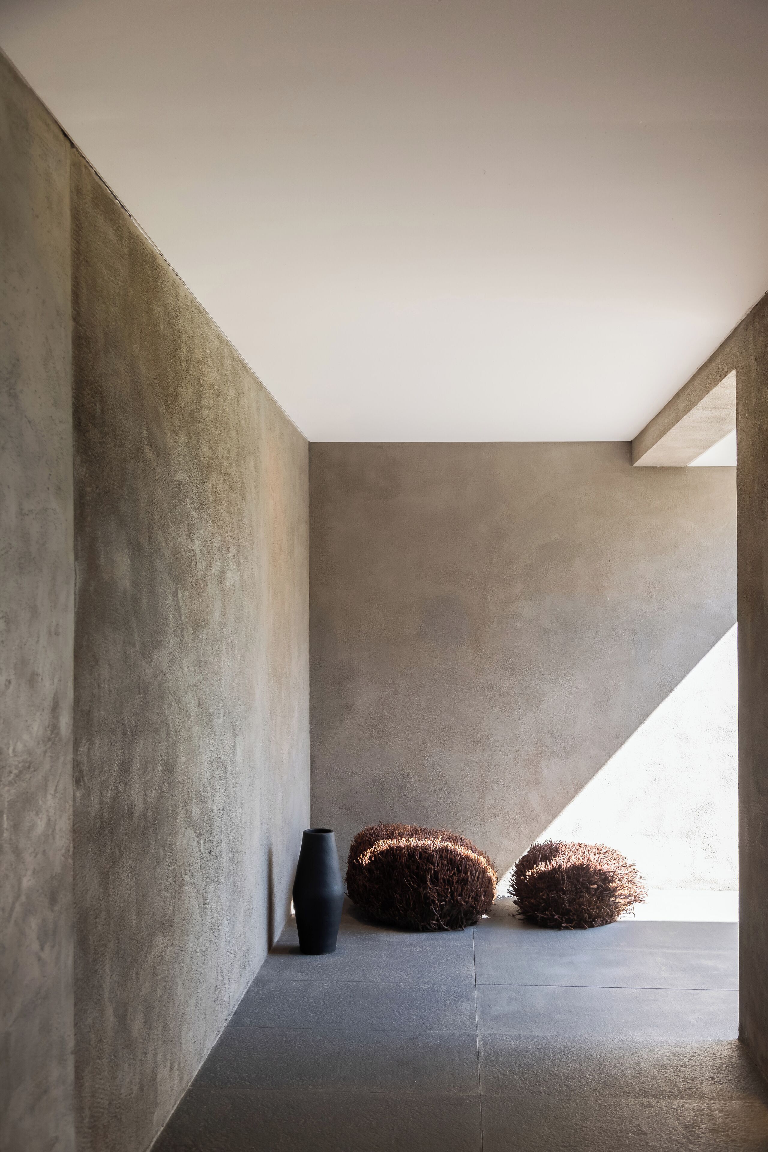 A minimalist room with a concrete wall, a black vase, and two textured poufs.