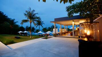 A modern outdoor lounge area with a covered seating area, palm trees, and umbrellas.