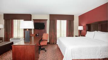 A hotel room with a bed, desk, chair, TV, and lamps.