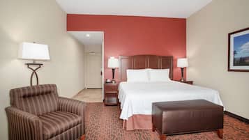 A hotel room with a bed, a chair, a bench, and two bedside tables with lamps.