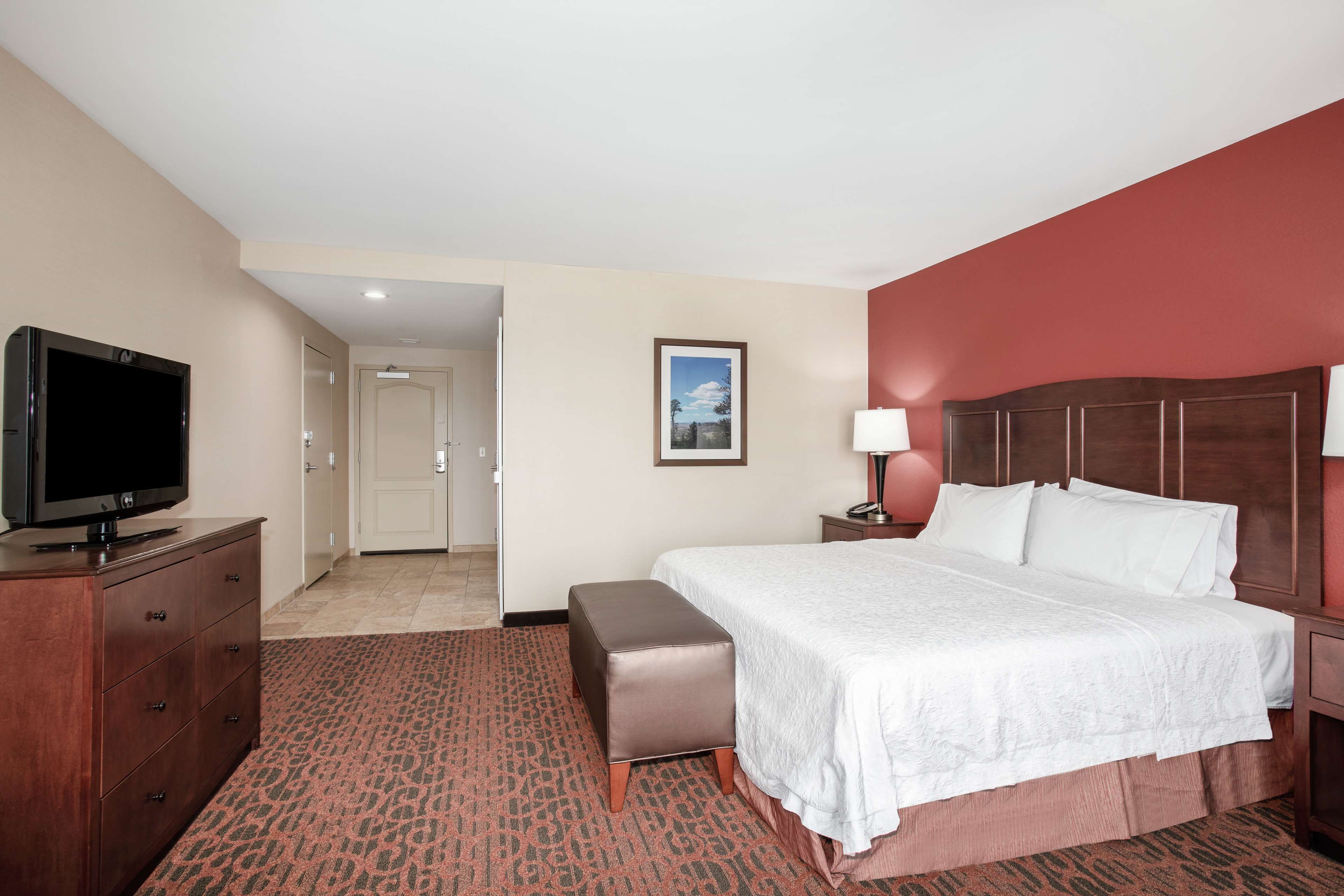 A hotel room with a bed, a television, a desk, and a door leading to another room.