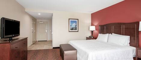 A hotel room with a bed, a television, a desk, and a door leading to another room.