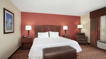 A hotel room with a large bed, two bedside tables with lamps, a chair, and an air conditioning unit.