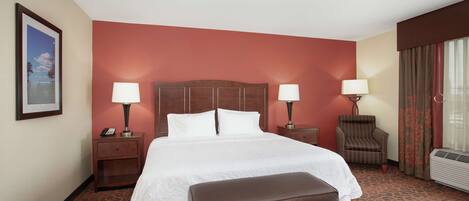 Quarto de hotel com uma cama grande, duas mesas de cabeceira com abajures, uma cadeira e um aparelho de ar condicionado.