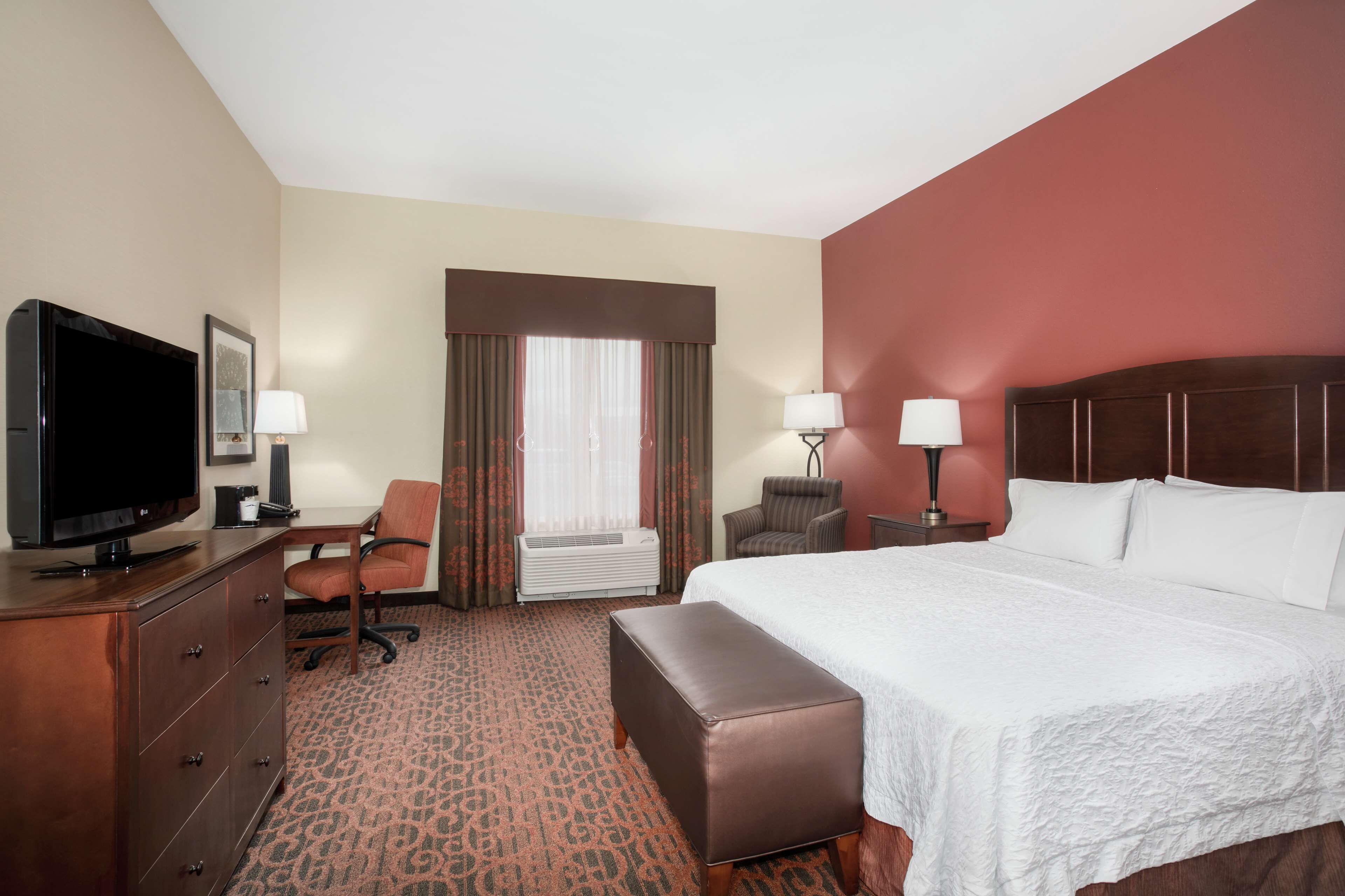 A hotel room with a large bed, a television, a desk, and a chair.