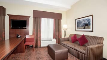 Habitación de hotel con televisión de pantalla plana, escritorio, silla, sofá, reposapiés, lámpara y un cuadro en la pared.