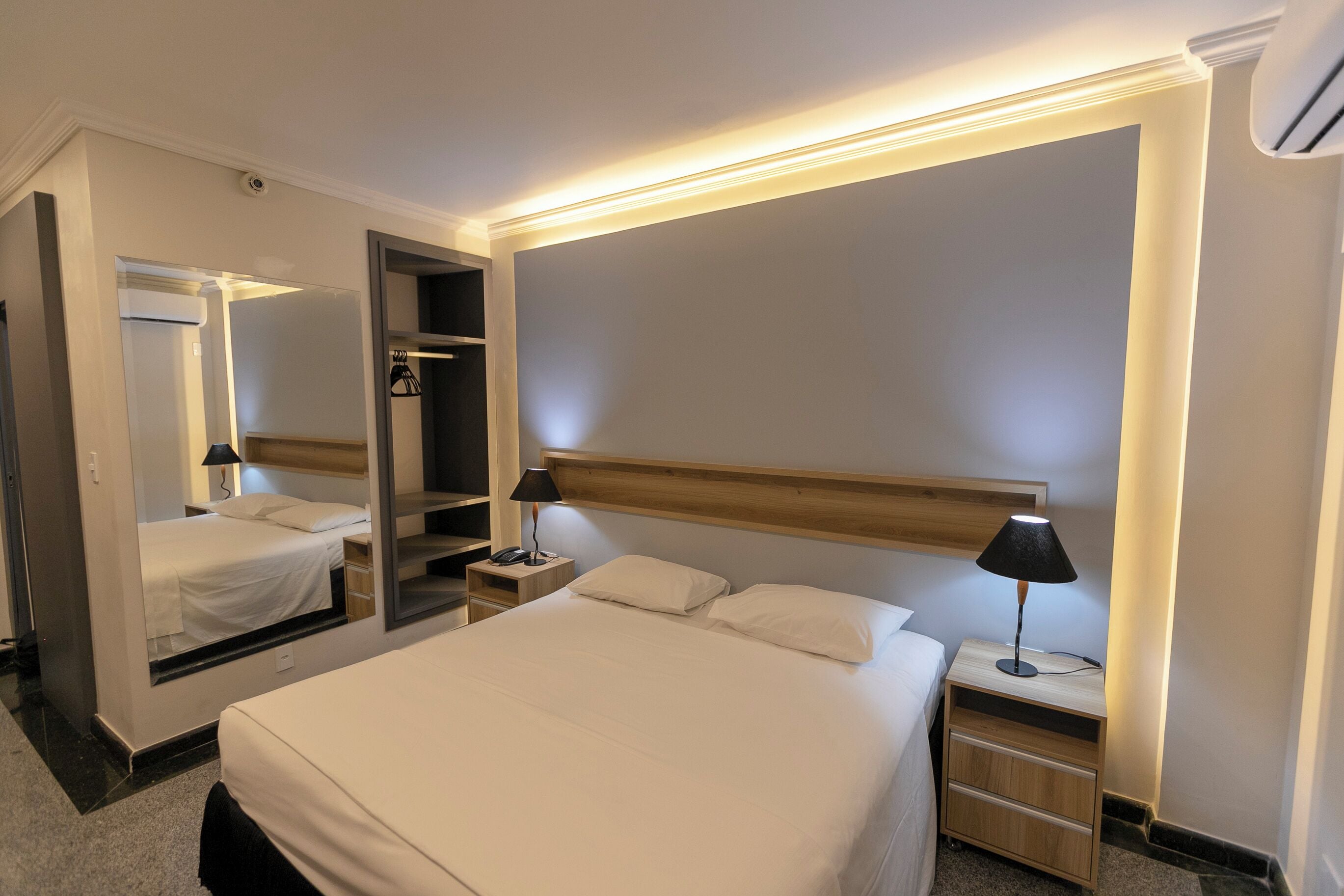 Una habitación de hotel con una cama grande, una mesita de noche con lámpara, un espejo y un armario.
