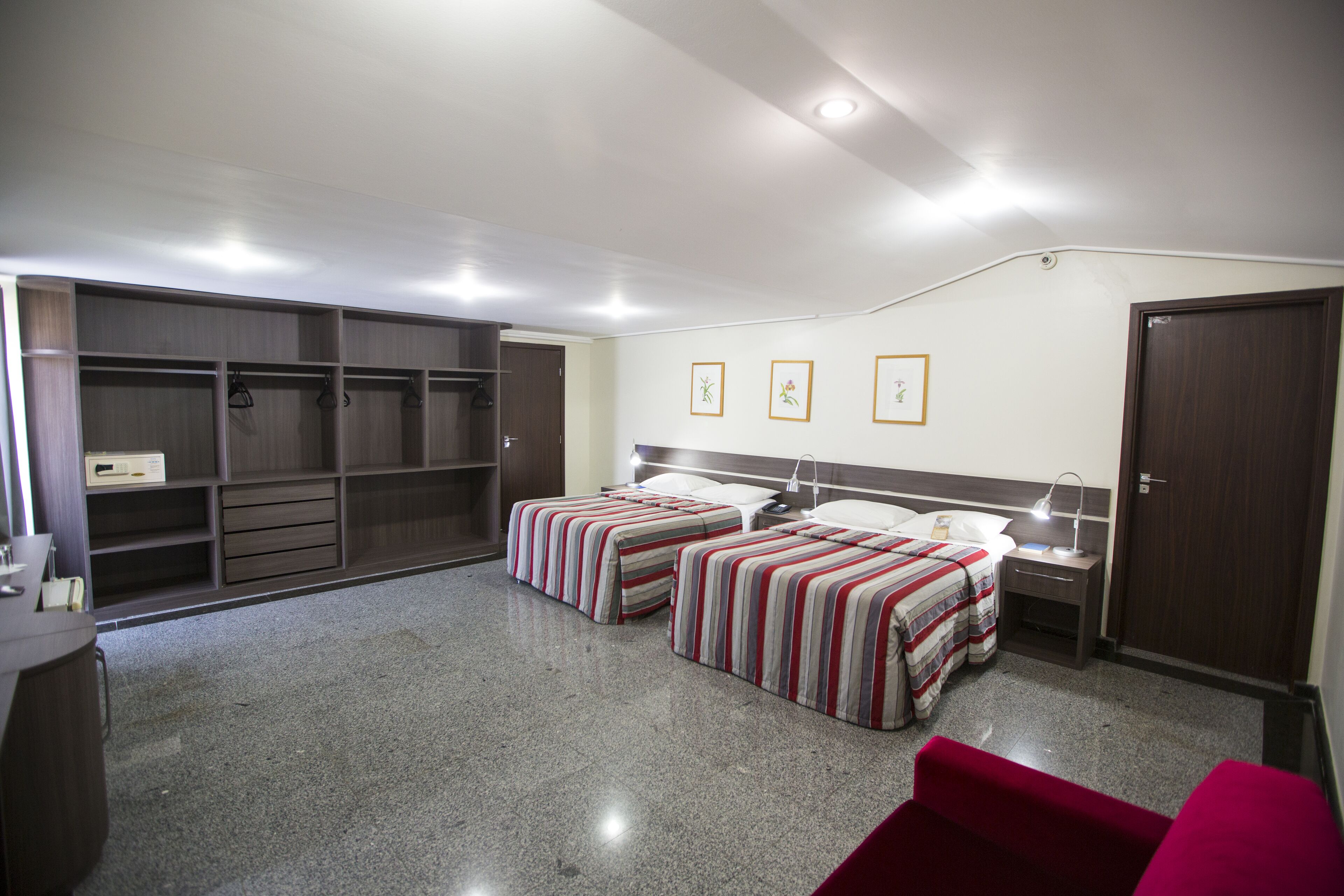 A bedroom with two beds, a wardrobe, a desk, and a red chair.