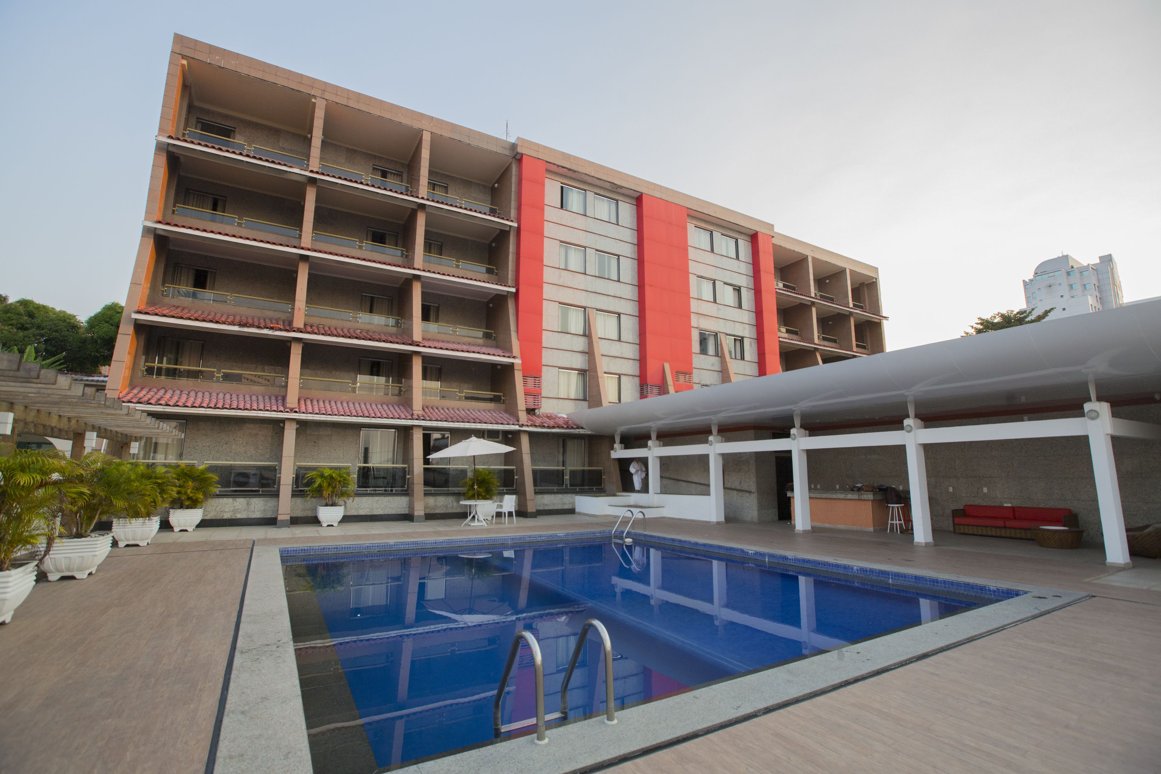 A multi-story building with a swimming pool, outdoor seating, and potted plants.