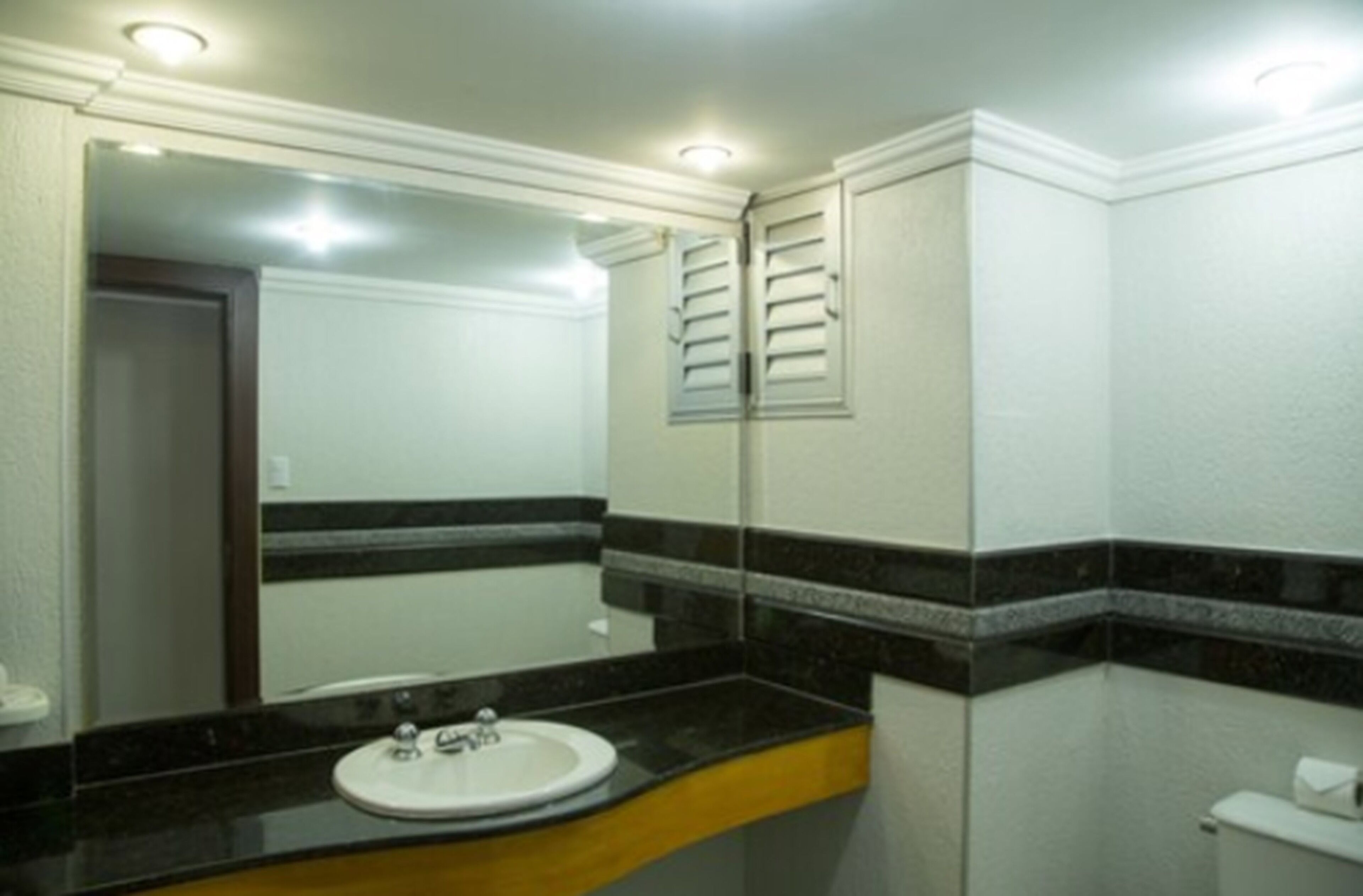 Un baño con lavamanos blanco, espejo y retrete.