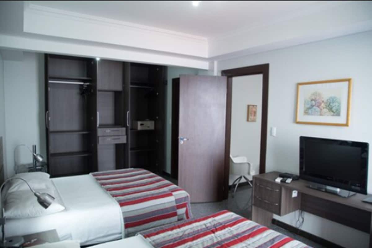 A hotel room with two beds, a wardrobe, a desk with a TV, and a chair.